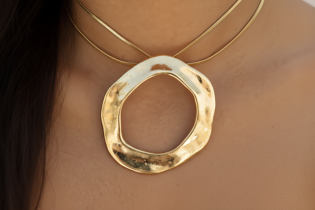 A person showing off their gold-colored open circle statement necklace with a ridged texture and two chains.